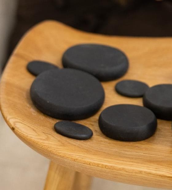 Smooth black massage stones arranged on a wooden stool