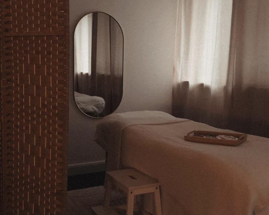 The treatment room: a massage couch with a cream cover, an oval mirror and soft curtains